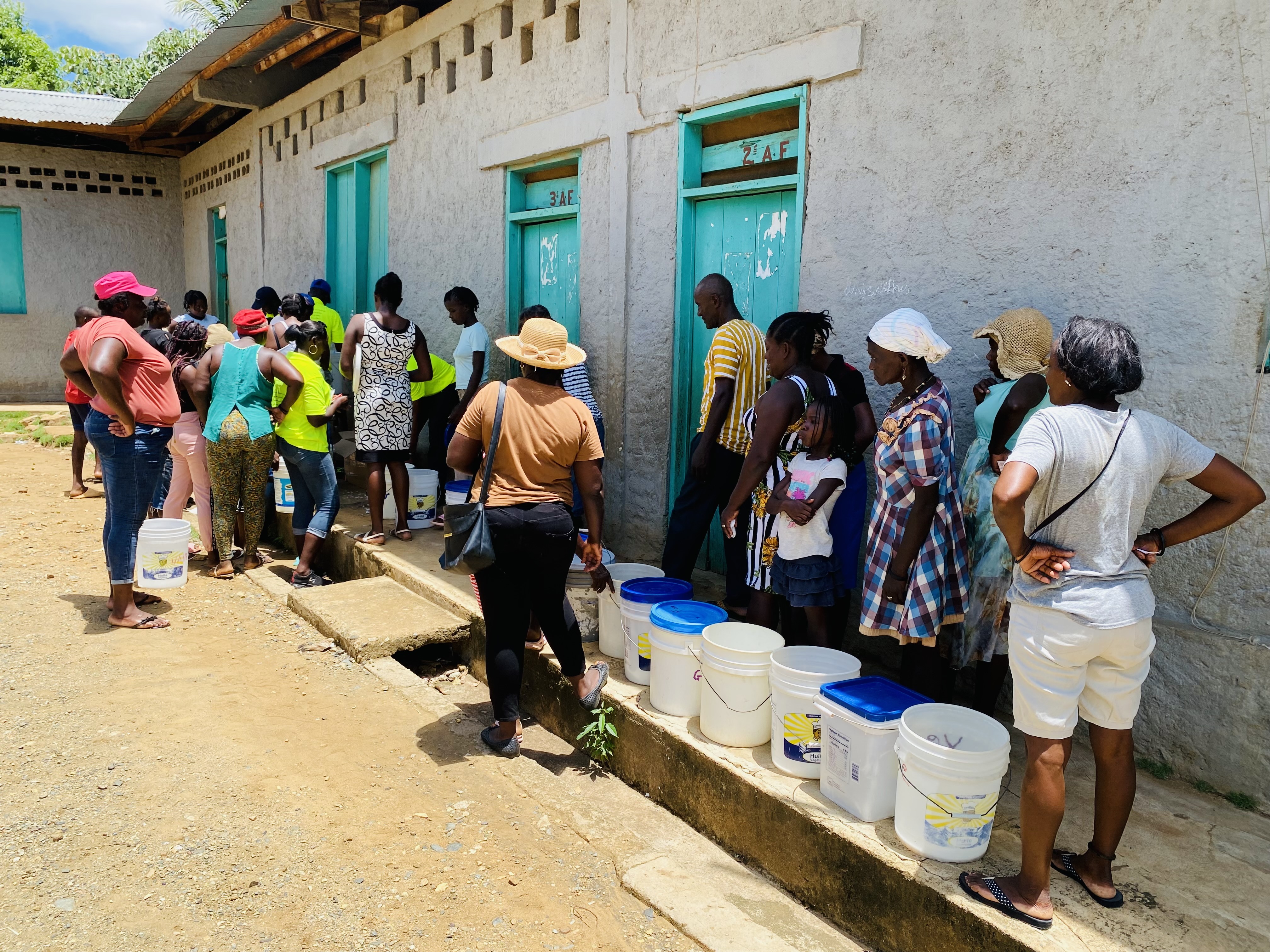 Villagers find shade while waiting their turn in line